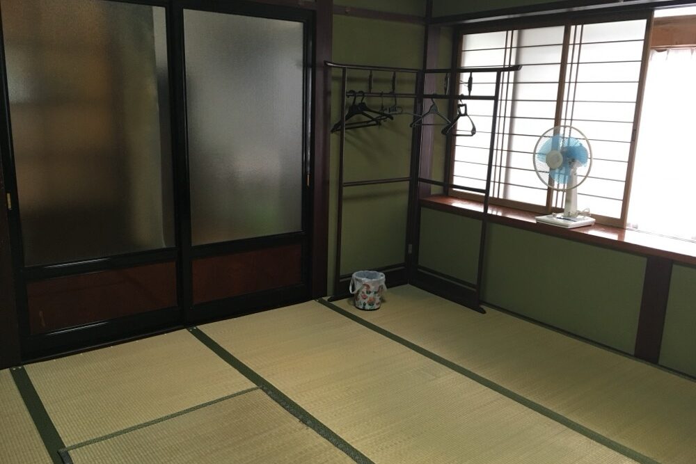 客室の写真。衣服をかける木製の家具にハンガーが5つかかっています。ゴミ箱と扇風機も写っています。